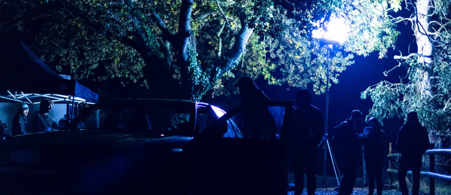 a group of people standing around a car with trees in the back